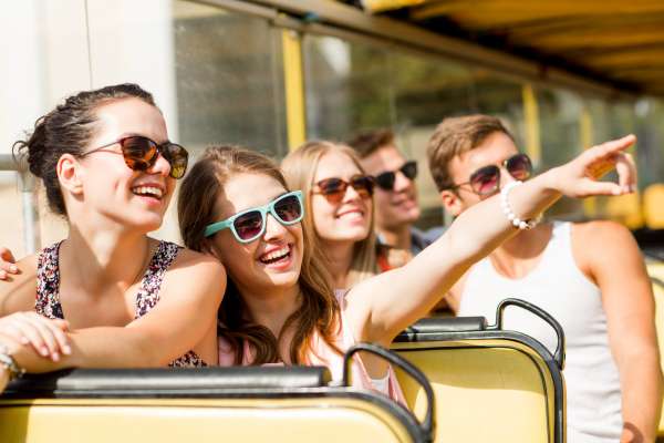 friendship, travel, vacation, summer and people concept - group of smiling friends traveling by tour bus