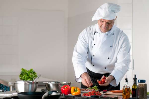 Dinner preparation at restaurant Happy smiling mature chef preparing a meal with various vegetables